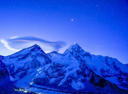 Base Camp lights shining as stars descend on Mount Everest.